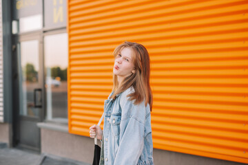 Fototapeta premium blonde teenager girl in a yellow dress and jute stands near an orange wall and spreads her arms.