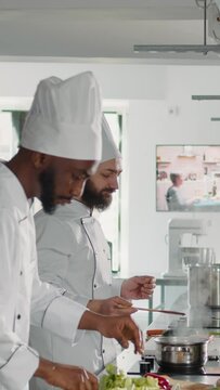 Vertical video: Male cook doing taste test with delicious sauce on stove, testing soup to make gourmet meal in kitchen. Professional chef using culinary recipe with ingredients for gastronomy