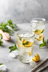 Lemonade summer iced cocktail with lemon and mint and paper straws on light gray background