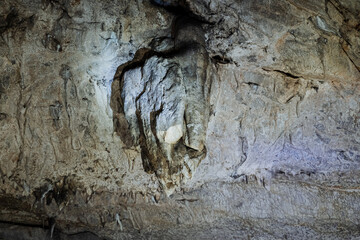 A stalactite hangs on the ceiling of the cave vault deep underground, the cave illuminated by the light of a lantern.