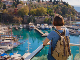 travel to Turkey, old town Antalya Kaleci. Happy asian female tourist traveller with backpack walks in old city. Woman on lookout over the old town and the port from viewpoint - obrazy, fototapety, plakaty