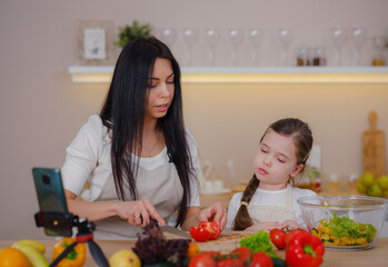 Obraz na płótnie Canvas Happy mother and daughter enjoy prepare freshly salad together in kitchen. Healthy food at home. Healthy Lifestyle and Eating Concept. little influencer filming blog about healthy eating