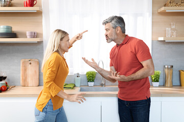 Fototapeta premium Emotional couple having quarrel at kitchen, shouting and gesturing