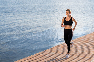 Morning Jogging. Beautiful sporty woman running outdoors on wooden pier along river
