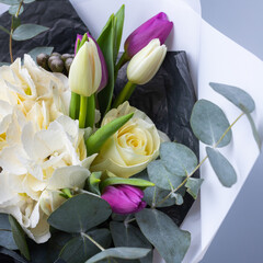 Close up of half bouquet of tulips, white hydrangea and eucalyptus twigs on blue background.