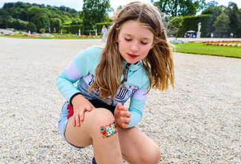 A little girl child fell and hurt her leg. The wound on the knee is sealed with a band-aid.