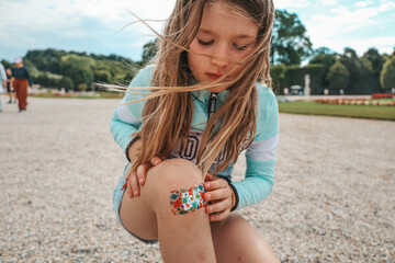 A little girl child fell and hurt her leg. The wound on the knee is sealed with a band-aid.
