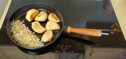 Ukrainian dumplings with stuffing are fried together with onions in a cast-iron frying pan. The...