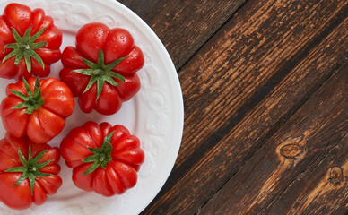 Fresh red tomatoes raf, on white plate on wooden background. Food concept