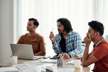 Group of serious developers listening to speech of collegue at meeting