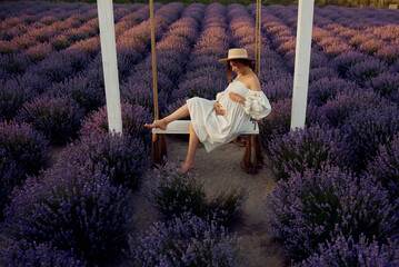 young beautiful pregnant girl on a swing in a lavender field at sunset