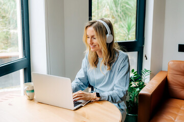 Cute blond woman is working on a laptop at home at the table.
