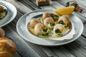 Prepared snails with butter sauce, white bread and spice on white salty plate on wooden background. Snails baked with sauce, Escargot Snails.