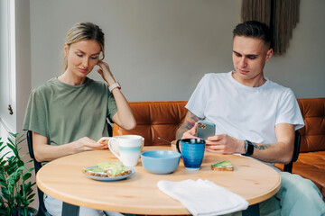 A man and a woman are using mobile phones for social networks while having breakfast.