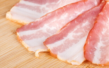 slices of raw bacon on a cutting board with basil, isolated on a white background