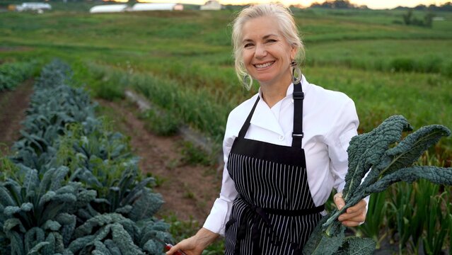 Portrait Of Smiling Blonde, Female Chef Picking Fresh Kale For A Farm To Table Restaurant.