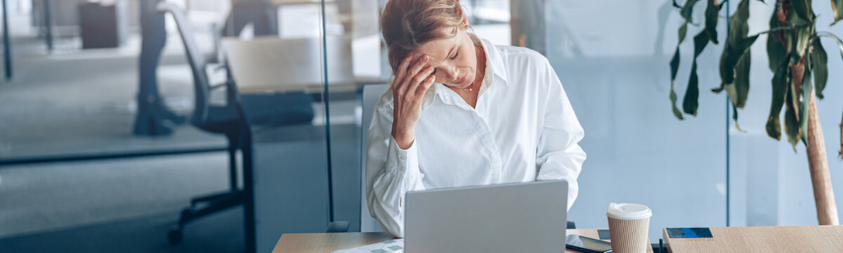 Tired businesswoman with headache working on laptop at her workplace at modern office.