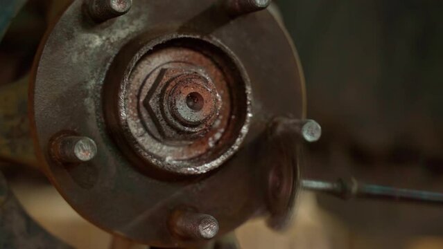 An auto mechanic cleans a spacer on a car hub from rust with a metal brush with a drill before replacing a brake disc on a car. Close-up.