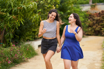 Two smiling friends running together hand in hand in the park