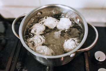 Chicken white big eggs are boiled in boiling water in a metal old pan on the stove in the kitchen, top view. Morning breakfast, food photography, concept.