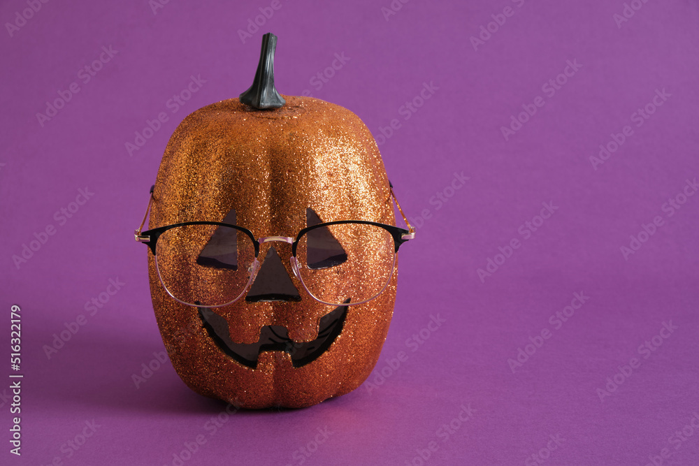 Wall mural trendy stylish glasses on the face of a decorative shiny orange pumpkin on a purple background