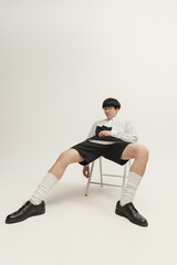 Portrait of stylish young boy sitting on chair, posing isolated on grey studio background Model wearing black and white outfit