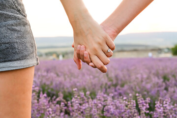 Two people in love hold hands in a lavender field against the backdrop of a sunset.