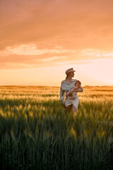 Naklejka na ściany i meble A portrait of young mother with a baby in her arms at sunset in the field. happy family concept