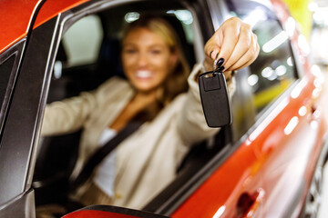 Portrait of a businesswoman holding the keys to her new car.  Young happy woman showing the key of...