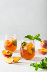 Summer cold peach fizz cocktail or iced tea with mint. Two glasses with peach lemonade on a white...