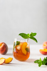 Homemade iced lemonade with ripe peaches and fresh mint. Fresh peach ice tea in a glass on a white background with ingredients. Summer refreshing beverage recipe. Bar, cafe menu. Copy space