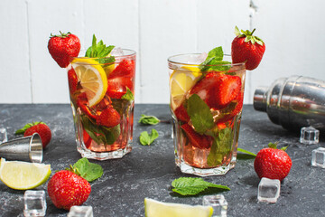 Summer refreshing mojito cocktail with strawberry, mint and lime with shaker for whipping drinks on a dark stone table