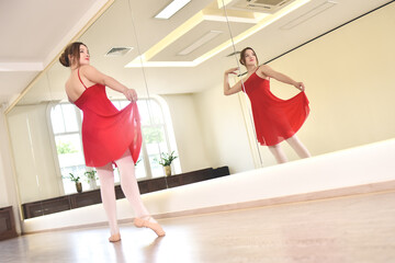 young ballerina in a red dress and pointe shoes performs exercises in a dance studio