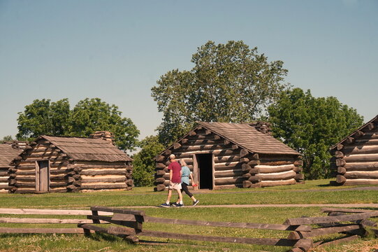 Two People Walking By a Row of Log Cabins at Valley Forge National Park in Summer Sunlight