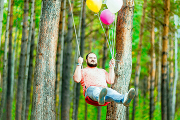 Fat funny man on a swing with balloons. Return to childhood.