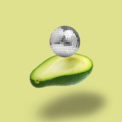 A disco ball flies out of an avocado half. Collage made out of half ripe fresh green avocado and...