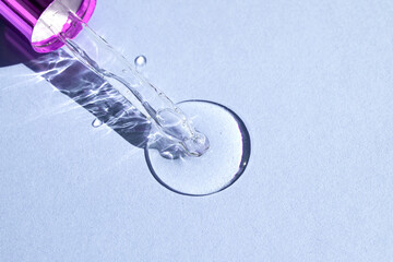 Glass pipette with air bubbles spilling drops of transparent moisturizing lotion on violet background.Top view, place for text.