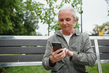 Fototapeta premium Old man browsing app on smartphone, outdoor in park