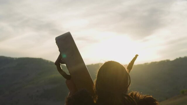 Silhouette of shaman playing ceremonial tambourine greeting new day at sunrise against mountains backside view. Siberian land mystical rituals