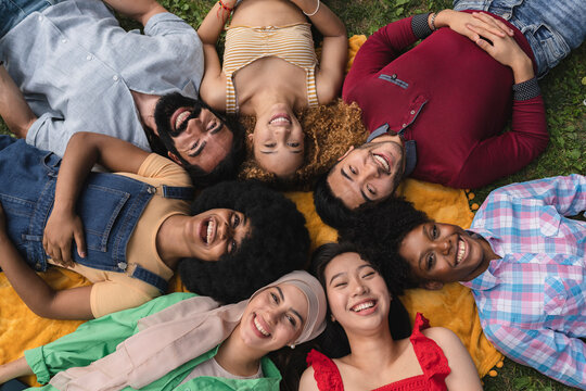 smiling group of multi-ethnic friends lie in a circle on the grass. - picnic concept -
