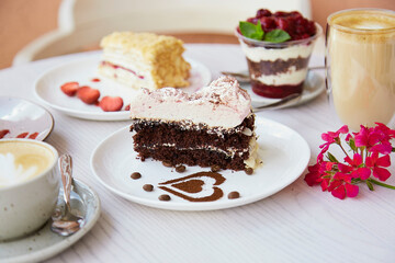 Natural vegan, layered desserts, piece of cakes with fresh fruits and berries outside and glass of latte. Celebration, assortment of sweets on the terrace