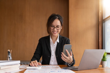 Asian woman holding smart phone while using calculator for business financial accounting calculate money bank loan rent payments manage expenses finances taxes doing paperwork concept, close up.