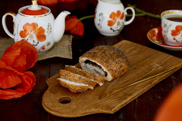 Traditional poppy seed bun with cup of tea and milk near poppies flowers and dishes with poppies ornaments. Delicious breakfast in summer. Lifestyle photography