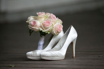 Closeup shot of a bridal bouquet of roses in white bridal shoes on a wooden floor