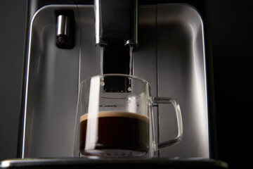 Freshly brewed coffee is poured from the coffee machine into glass cups.