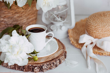 A beautiful postcard. A white coffee cup with a saucer, candles and a vase with a bouquet of white peonies. Beautiful still life. Spring, summer time. The concept of 