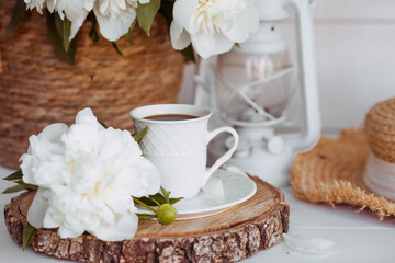 A beautiful postcard. A white coffee cup with a saucer, candles and a vase with a bouquet of white peonies. Beautiful still life. Spring, summer time. The concept of 