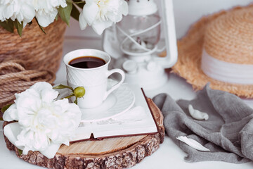 A beautiful postcard. A white coffee cup with a saucer, candles and a vase with a bouquet of white peonies. Beautiful still life. Spring, summer time. The concept of 