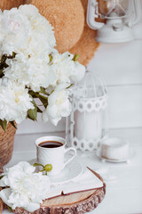 A beautiful postcard. A white coffee cup with a saucer, candles and a vase with a bouquet of white peonies. Beautiful still life. Spring, summer time. The concept of 