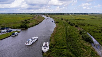 Aerial view of boats floating on river surrounded by greenery fields in Norfolk broads